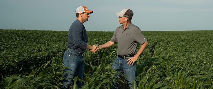 Farmer and agronomist shaking hands in a field